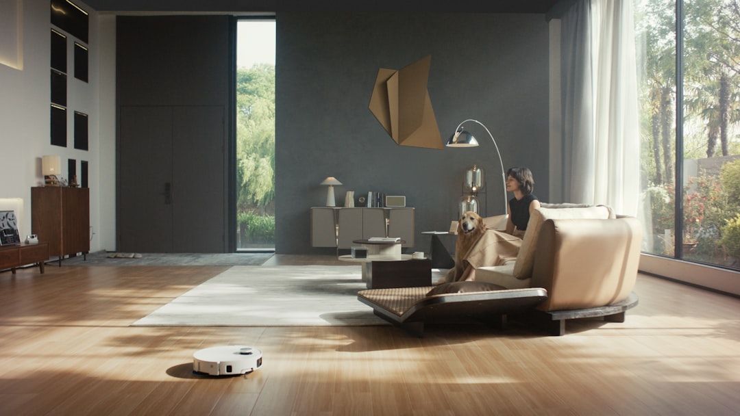 Dreame robot vacuum and mop is cleaning a spacious, modern living room as a woman relaxes with her pet dog on the sofa.